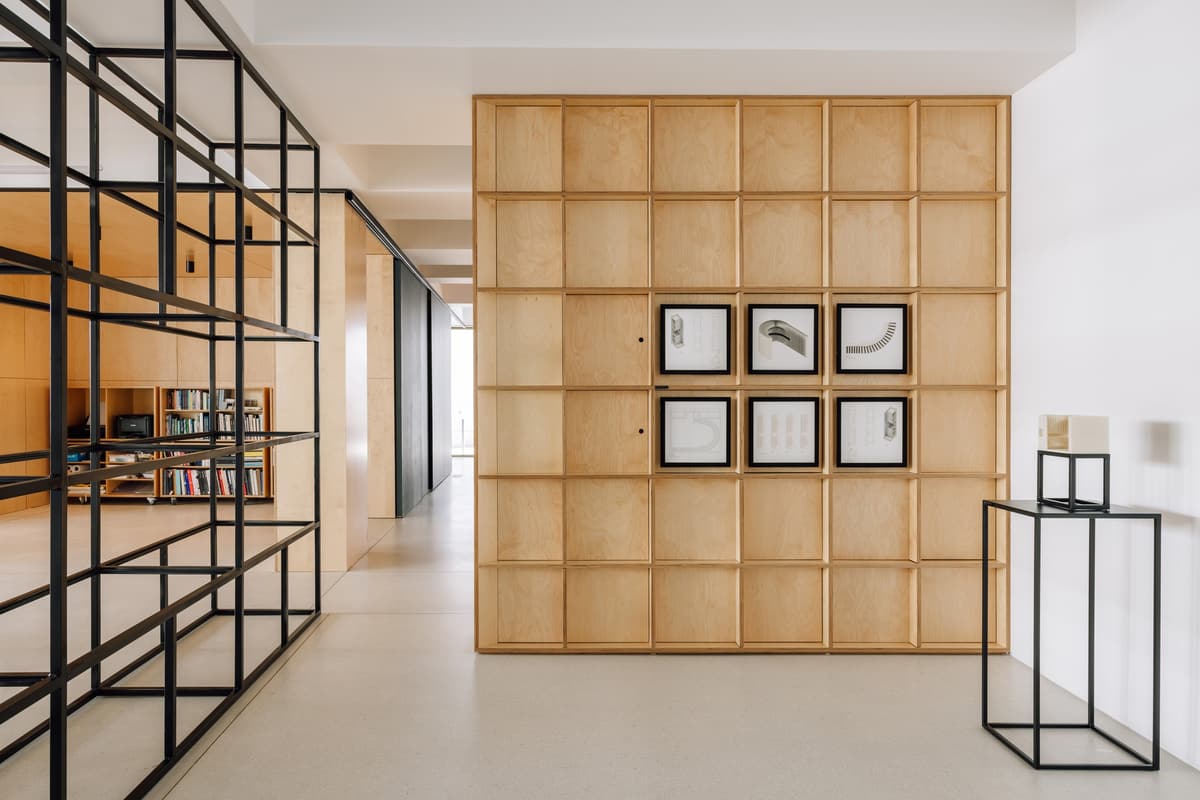 Plywood grid wall with framed drawings beside a black steel shelving frame in the NOZ studio