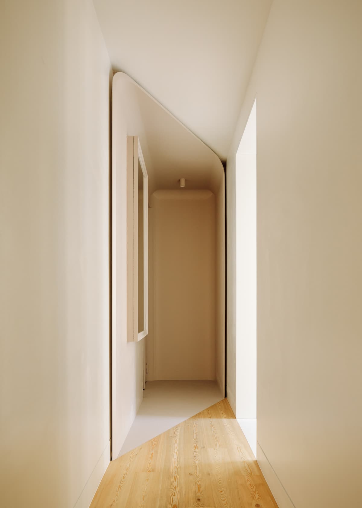 Corridor with pale walls and pine floor leading into the soft-toned entrance box with a framed mirror