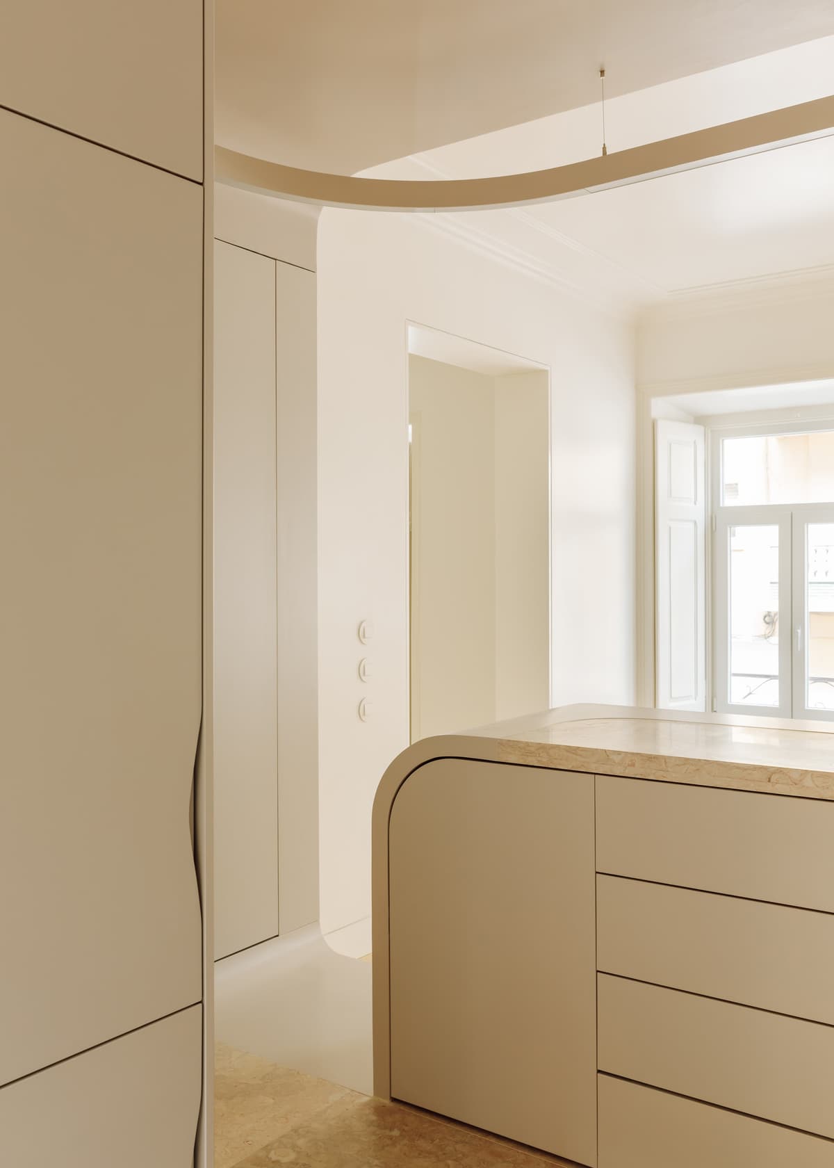 Kitchen island with rounded edge and stone top, looking towards a bright room with a tall window