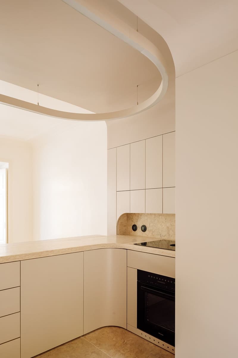 Kitchen corner with beige cabinets, curved stone worktop, built-in oven and a suspended curved light