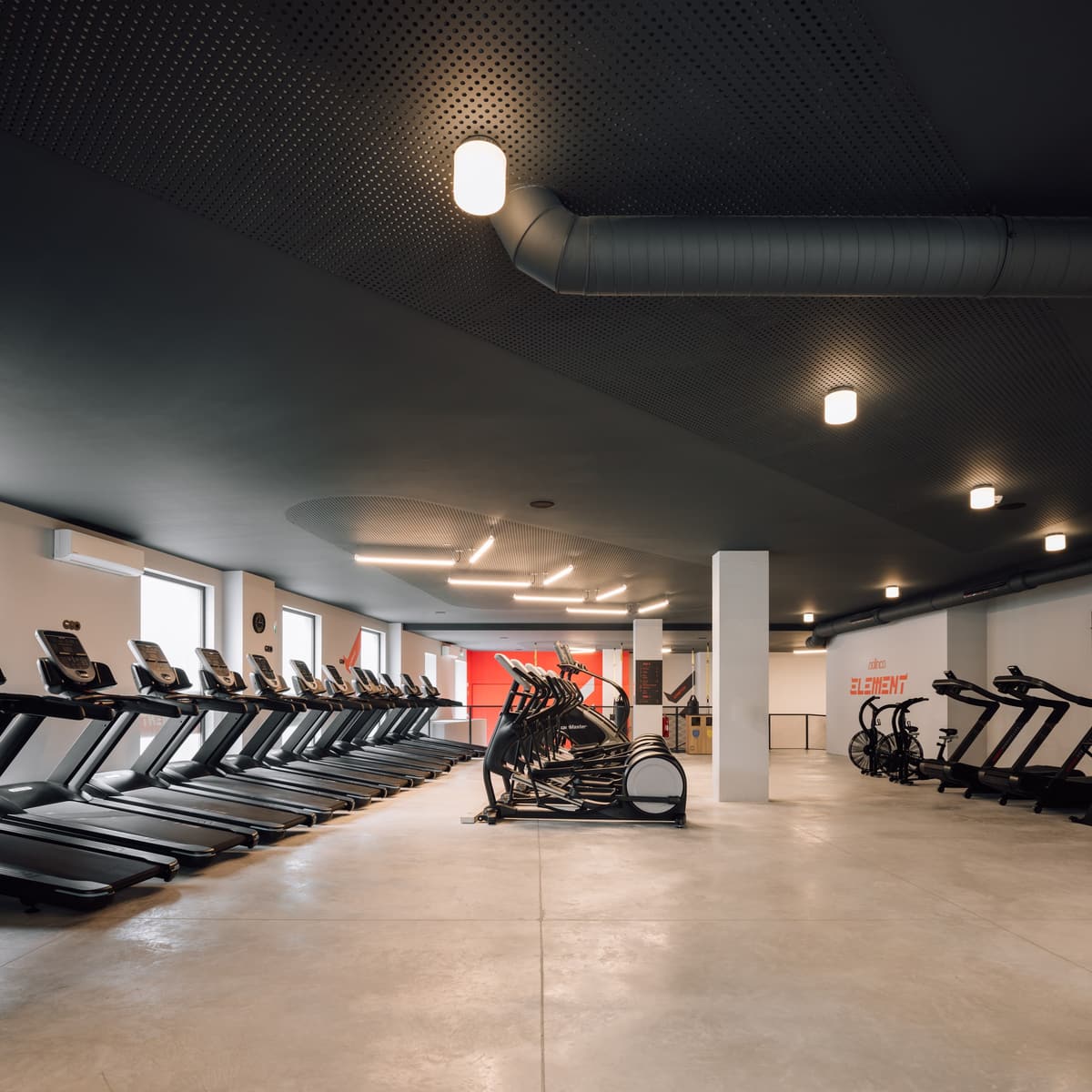 Element gym cardio floor with rows of treadmills, dark perforated ceiling, exposed ducts and concrete floor