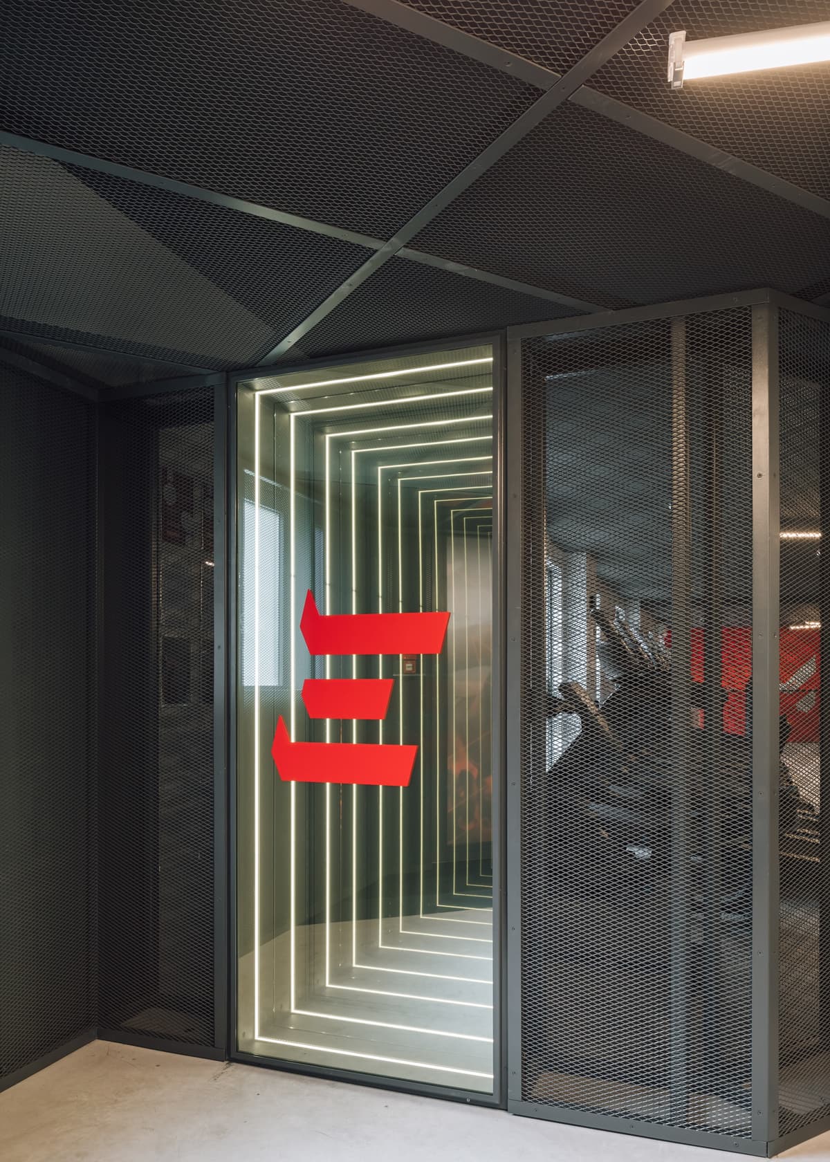 Gym entrance through an infinity mirror box of black metal mesh, with red arrow graphics on the glass