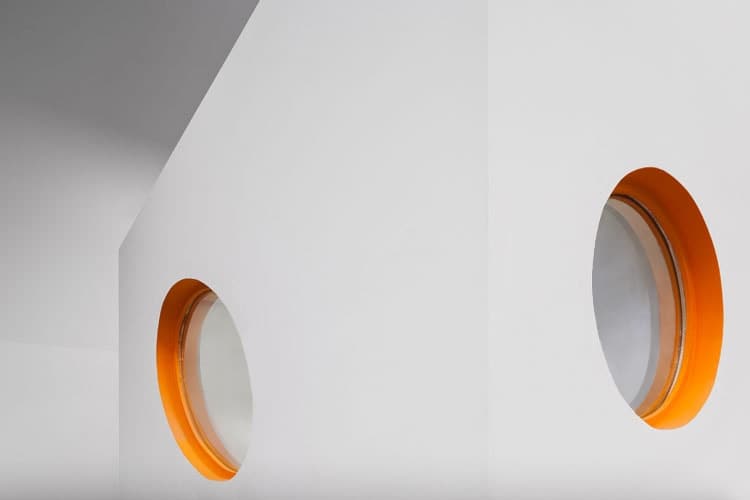 Two circular windows with bright orange reveals cut into white walls at the Pump gym in Republica