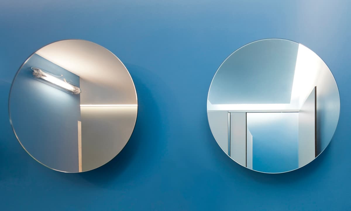 Two round mirrors on a blue wall reflecting white partitions and a fluorescent light at the Pump gym