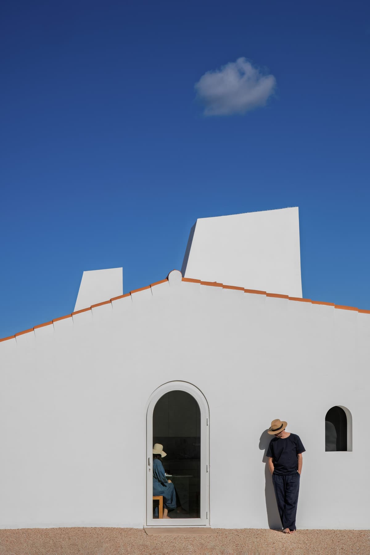 Whitewashed gable with arched door and window under a blue sky, white chimneys rising behind the roof