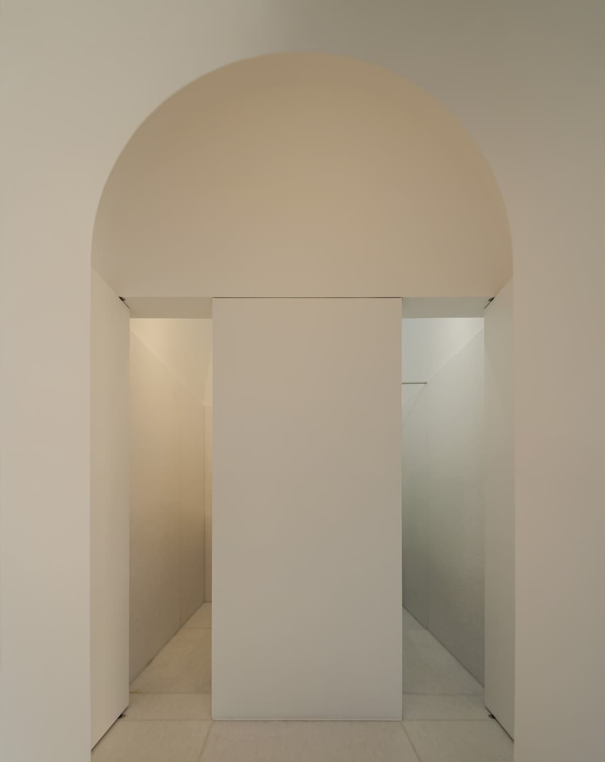 Arched white opening leading to two narrow passages divided by a central wall, in soft warm light