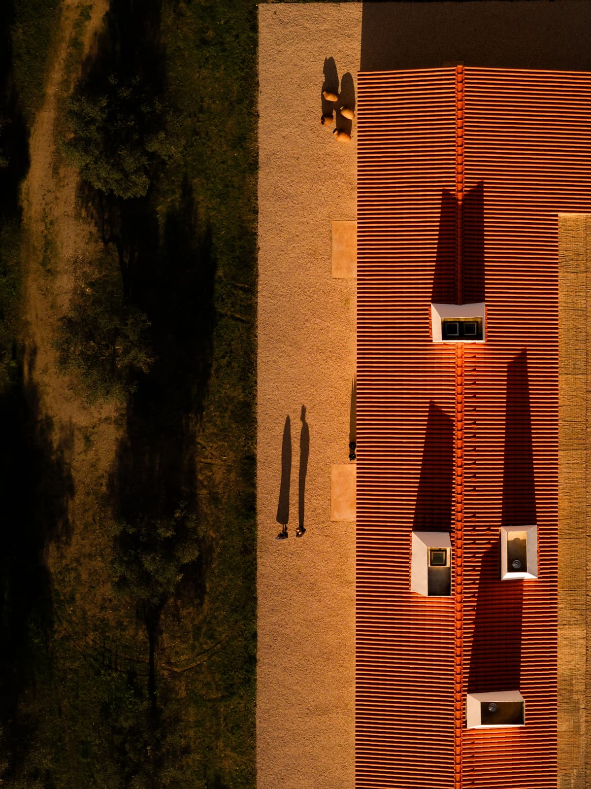 Top-down aerial view of the terracotta tile roof with white chimneys casting long shadows on gravel