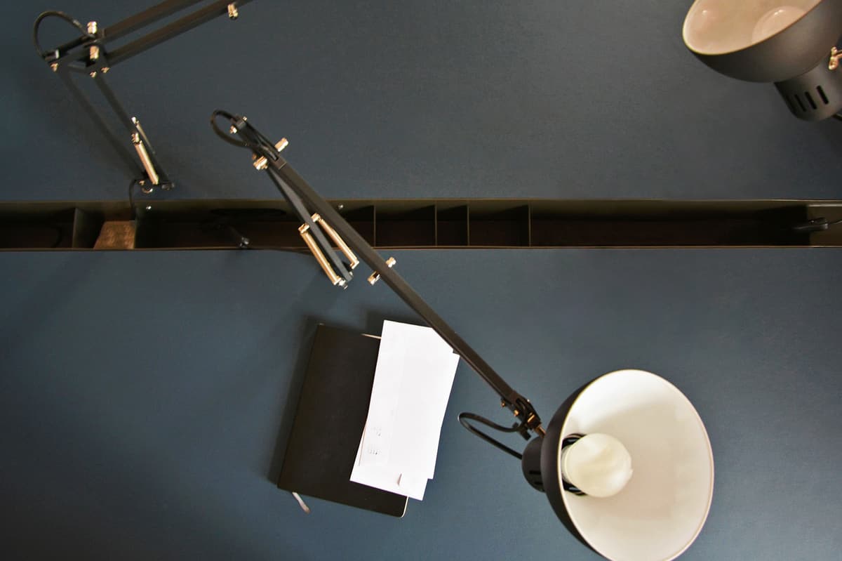 Overhead view of the grey-blue linoleum desk with black task lamps, notebook and divided cable gutter