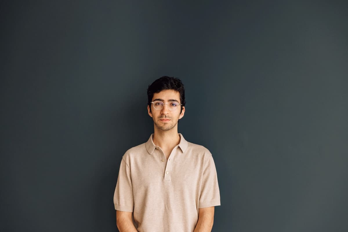 Portrait of francisco alves, in glasses and a beige polo shirt, against a dark grey wall