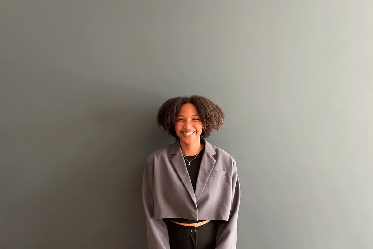 Portrait of mariana tavares, in a grey cropped blazer, against a light grey wall