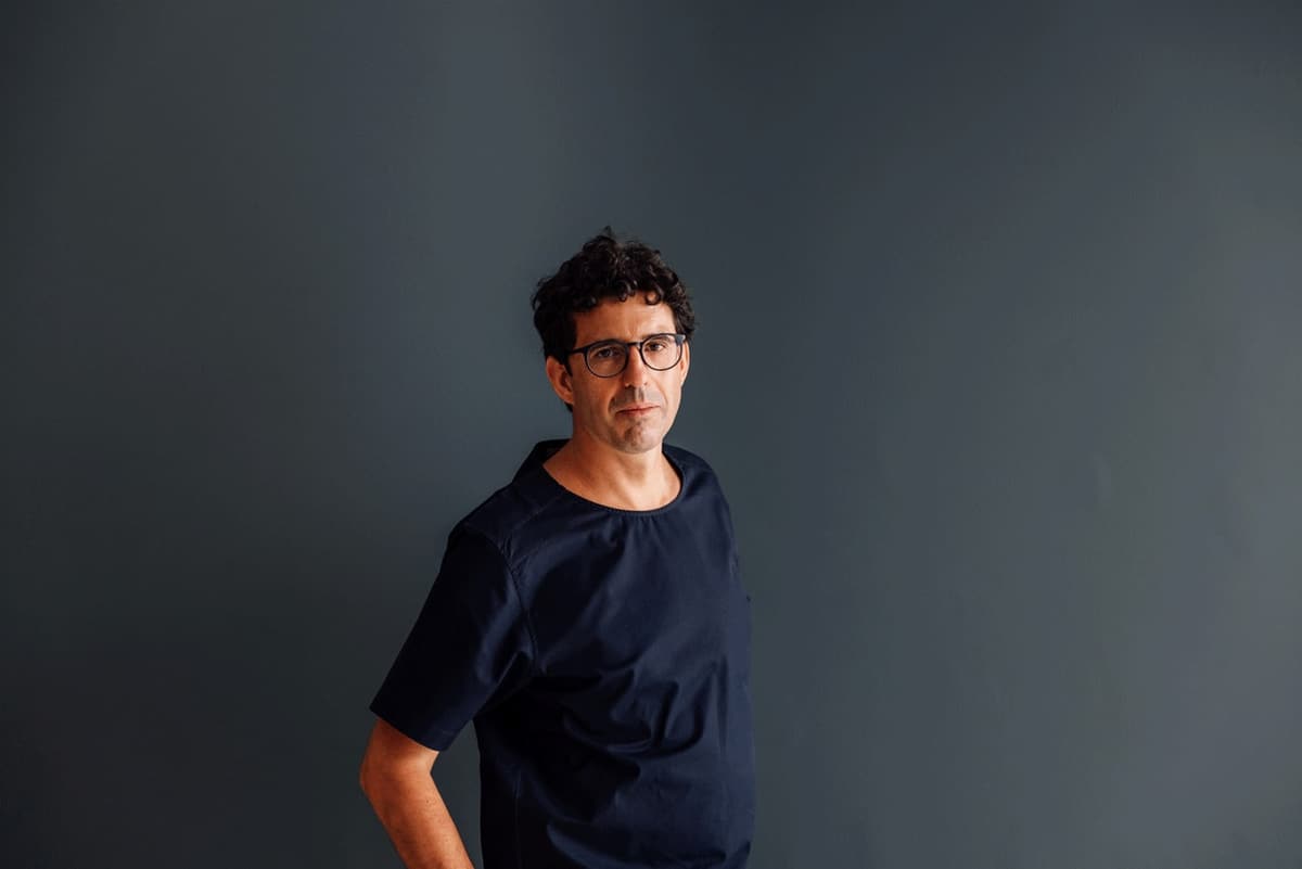 Portrait of rui dias, in glasses and a dark navy t-shirt, against a dark grey wall