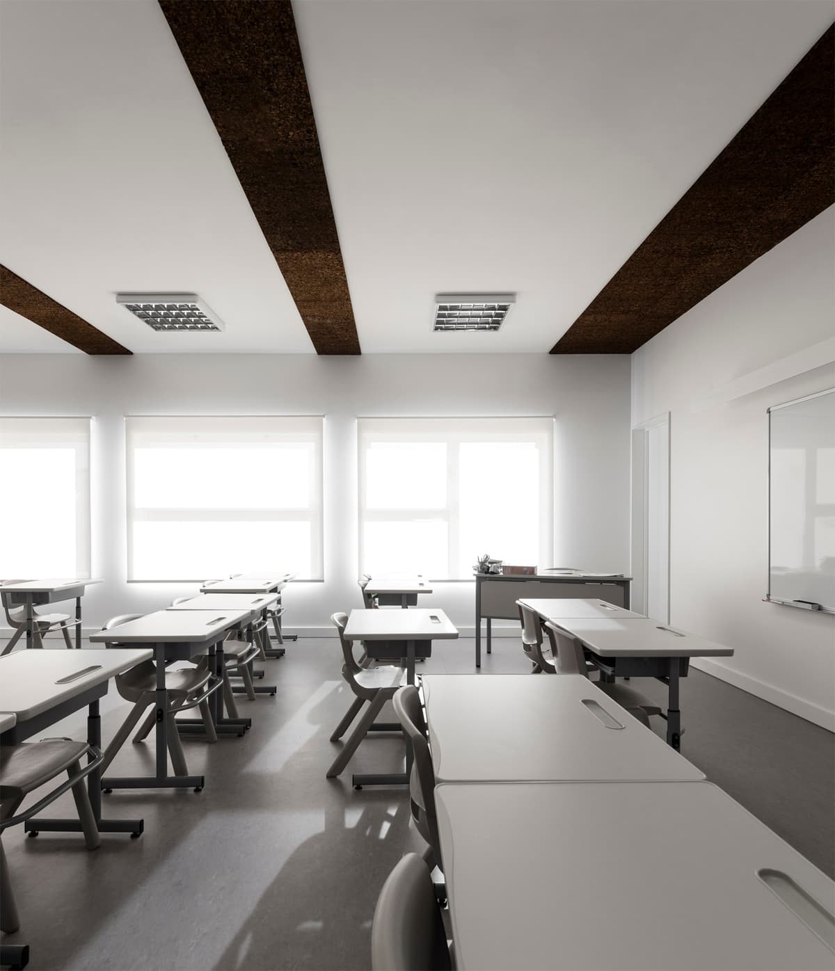 Classroom at Alguber school with white desks, dark ceiling strips and daylight through screened windows