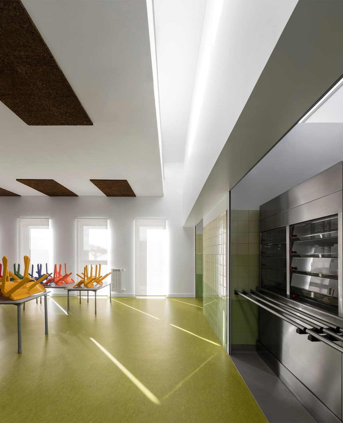 School canteen with green floor, dark ceiling panels, chairs stacked on tables and a stainless steel serving counter