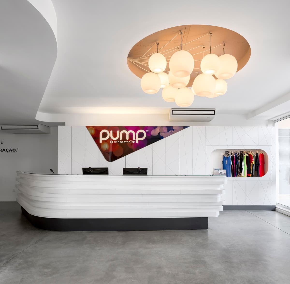 Reception at the Pump Alvalade gym with a layered white desk, backlit logo panel and a cluster of globe lights
