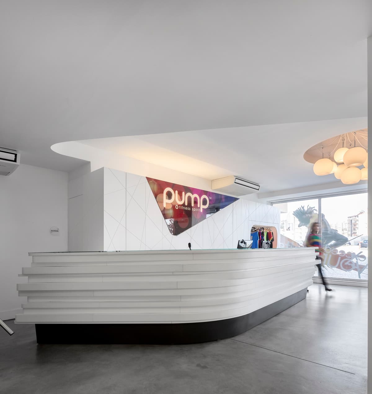 Side view of the curved layered reception desk at Pump Alvalade, with a person passing by the shopfront