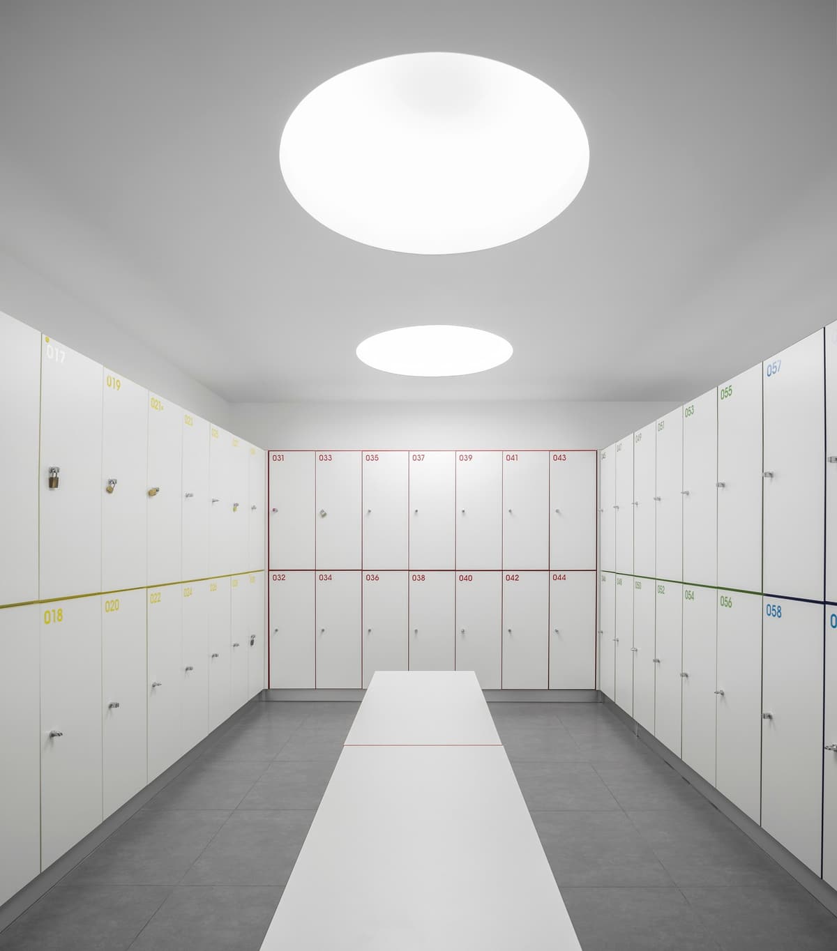 Pump Alvalade changing room with rows of numbered white lockers, a central bench and round ceiling lights