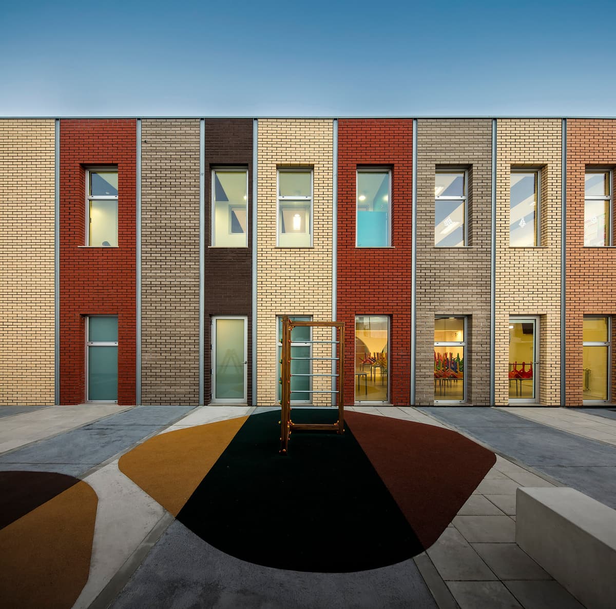 Murteira school extension with vertical bands of different coloured brick, facing a playground at dusk