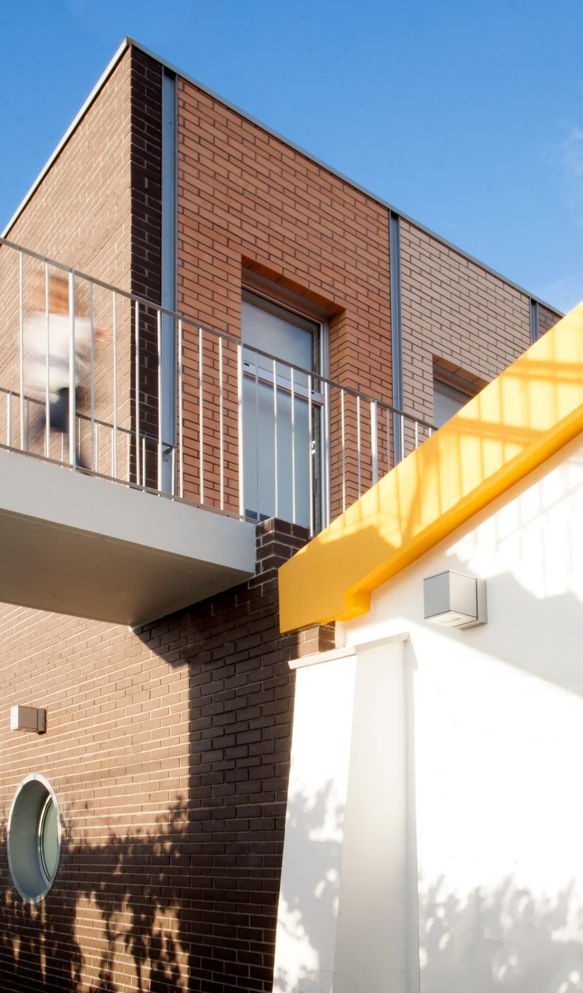 Brick extension with a steel balcony meeting the white walls and yellow trim of the original school