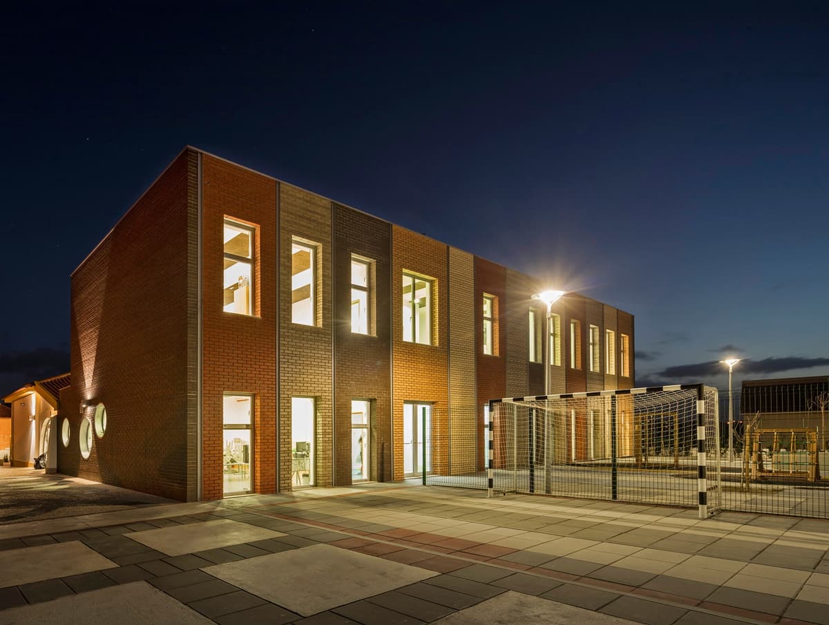 Night view of the lit brick classroom block with a football goal on the paved playground