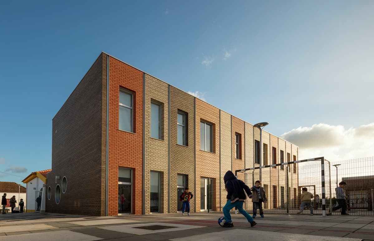Children playing football in front of the multicoloured brick extension in late afternoon sun