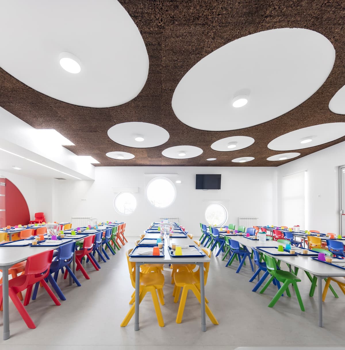 School canteen with colourful chairs, round windows and a dark textured ceiling with white circular panels