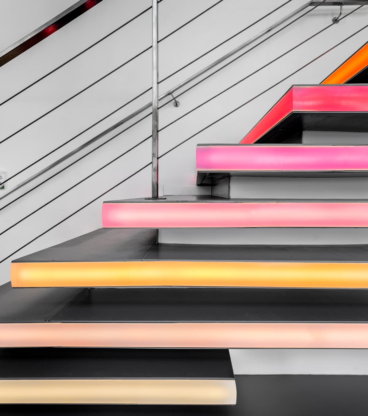 Detail of floating stair treads with illuminated edges in pink, orange and yellow at the Pump Expo gym