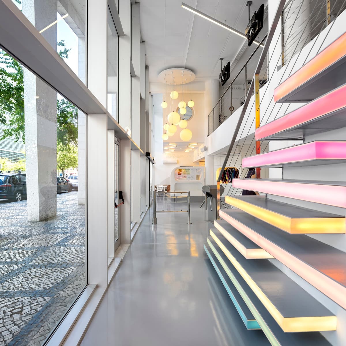 Double-height entrance at the Pump Expo gym with glazed facade, glowing stair treads and globe pendant lights