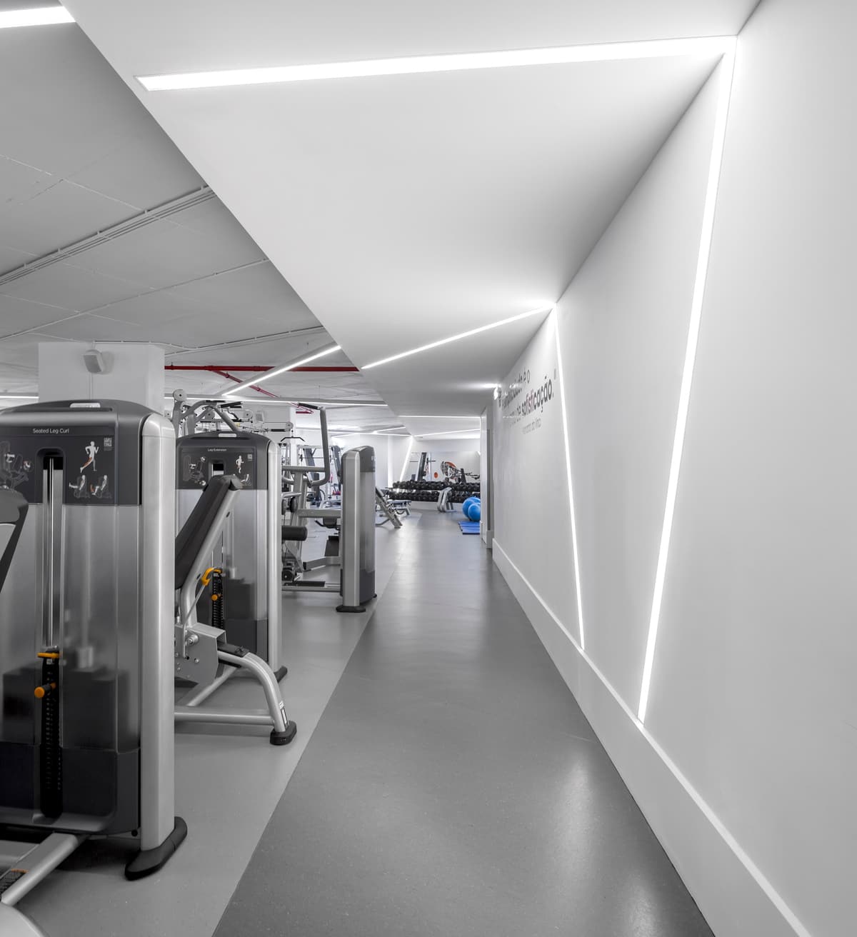 Training area at the Pump Expo gym with weight machines along a white corridor lined with angled light strips