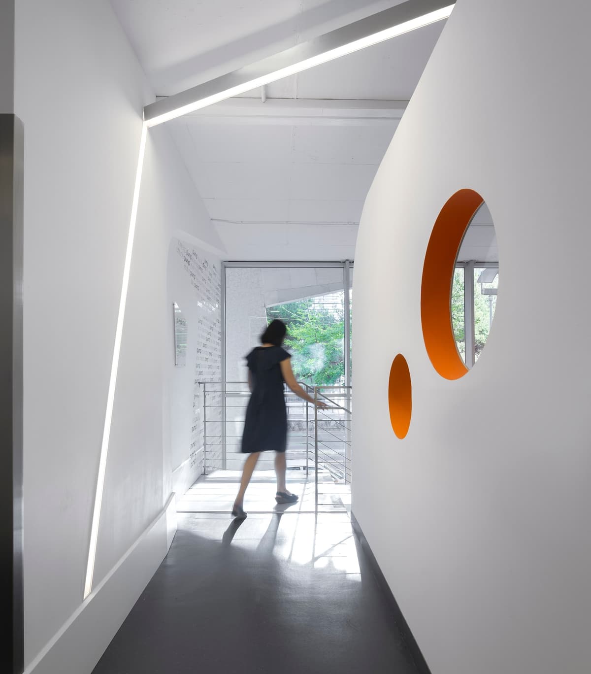 Person walking along a white corridor with an angled light strip and round orange-edged openings, Pump Expo gym