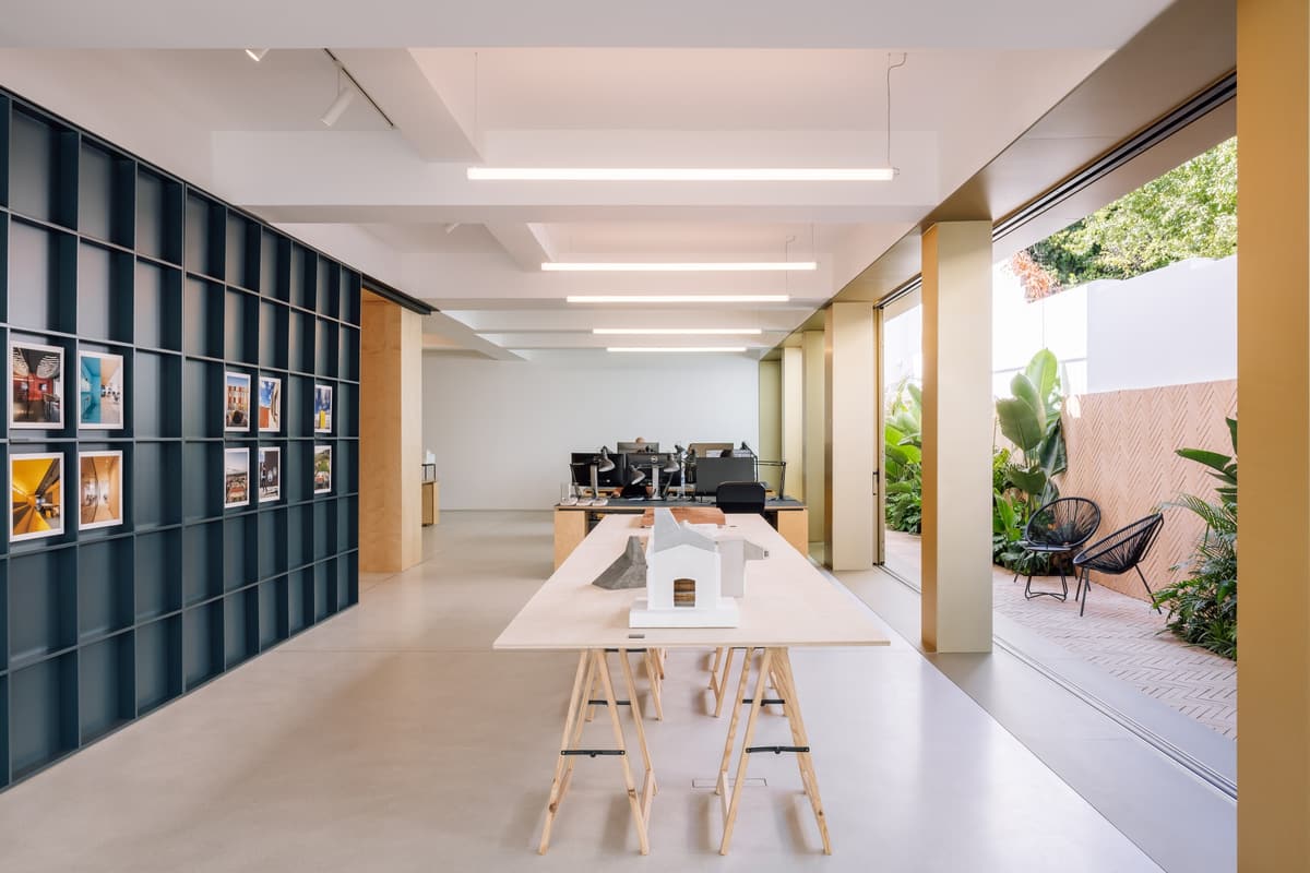 NOZ studio in Lisbon: long work table on trestles, dark blue shelving wall and a glazed façade open to a planted patio